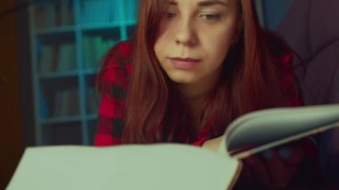 Güzel bir öğrenci büyük bir kitap okuyor. Düşünceli genç bir kadın elinde kitapla kanepede uzanıyor ve akşam karanlık bir odada kitap okuyor.