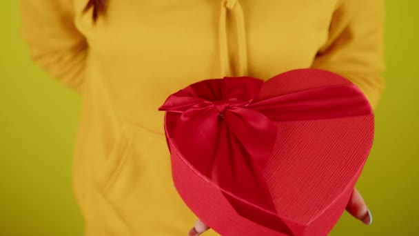 Sarı arka planda kırmızı kalp şeklinde hediye kutusu olan bir kadın vücudu. Tanınmayan biri romantik bir hediye daha alır. Sevgililer Günü ve Uluslararası Kadınlar Günü 'nde hediye kavramı. — Stok video