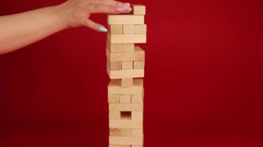 Kırmızı arka planda Jenga oyunu. İnsan eli küçük tahta blokları söker. Tanımlanamayan adam ve kadın oyun oynuyorlar Jenga. Evde boş zaman aktivitesi kavramı.