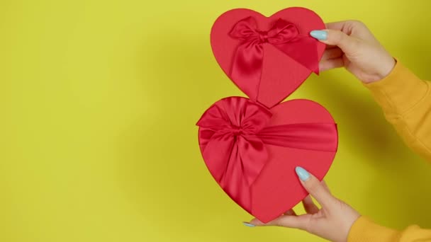 Womans hands with red gift boxes in form of heart on yellow background. Unrecognizable person holding romantic gifts with ribbon. Concept of present on valentine day and international womens day. — Stock Video