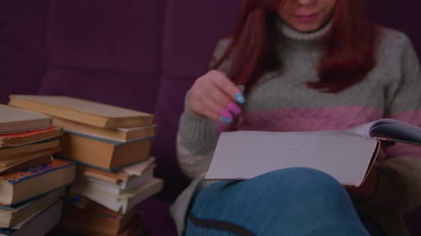 Lecture étudiante parmi les livres. Femme assise sur le canapé avec une pile de livres et un manuel de lecture — Video