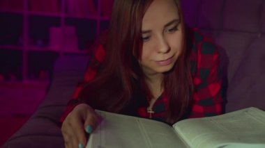 Güzel bir öğrenci büyük bir kitap okuyor. Düşünceli genç bir kadın elinde kitapla kanepede uzanıyor ve akşam karanlık bir odada kitap okuyor.