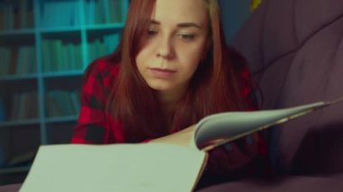 Güzel bir öğrenci büyük bir kitap okuyor. Düşünceli genç bir kadın elinde kitapla kanepede uzanıyor ve akşam karanlık bir odada kitap okuyor.