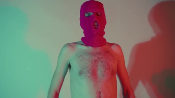 Porträtt av en anonym skjortlös man i Balaclava. Oigenkännlig bekymmerslös smal hane med naken överkropp i rosa balaklava stående nära väggen. — Stockvideo