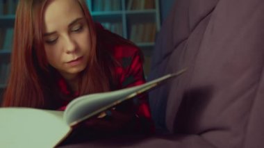 Güzel bir öğrenci büyük bir kitap okuyor. Düşünceli genç bir kadın elinde kitapla kanepede uzanıyor ve akşam karanlık bir odada kitap okuyor.