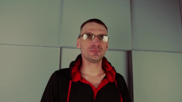 회색 기하학 벽 근처에서 안경을 쓴 말라깽이 남자. 평상복을 입고 카메라를 보고 스튜디오에서 포즈를 취하고 있는. — 비디오