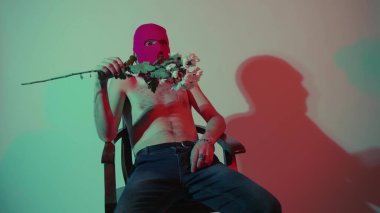 Kar maskeli, elinde çiçeklerle oturan isimsiz bir adam. Tanımlanamayan tehlikeli erkek pembe kar maskeli çıplak adam elinde bir buket beyaz çiçekle duvarın yanında oturuyor.