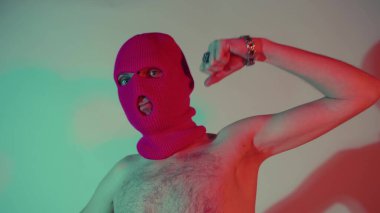 Kar maskeli, pazılarını gösteren isimsiz bir adam. Tanınmayan erkek, çıplak gövdeli, pembe kar maskesi takıyor, pazılarını gösteriyor ve gölgeyle duvarın yanında dikilirken kameraya bakıyor.