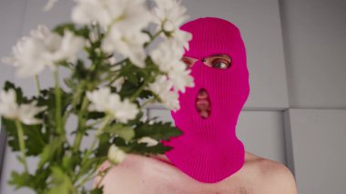 Çiçekli, kar maskeli, isimsiz bir adam. Tanımlanamayan, çıplak gövdeli, elinde beyaz çiçekler olan pembe kar maskeli, gri dokulu geometrik duvarın yanında duran tehlikeli bir erkek.