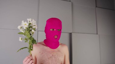 Çiçekli, kar maskeli, isimsiz bir adam. Tanımlanamayan, çıplak gövdeli, elinde beyaz çiçekler olan pembe kar maskeli, gri dokulu geometrik duvarın yanında duran tehlikeli bir erkek.