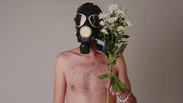 Un homme sans visage torse nu dans un masque à gaz avec des fleurs. Un homme méconnaissable avec un torse nu dans un masque à gaz noir avec un bouquet de fleurs blanches fraîches. Concept : allergie et pollution de l'environnement — Photo