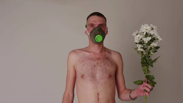 가스 마스크를 쓰고 꽃으로 얼굴을 가리지 않은 남자. 가스 마스크를 쓴 나체의 몸통을 가진 남자 신선 한 흰색 꽃 꽃다발 과 함께. 개념 : 알레르기 와 환경 오염 — 스톡 사진