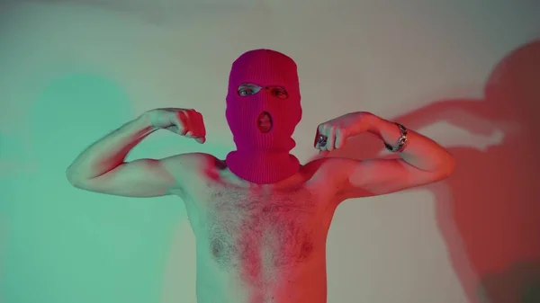 Nerozpoznatelný člověk v růžové kuklě ukazuje sílu s rukama. Křehké a tenké mužské show biceps, stojící — Stock fotografie