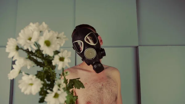 Egy férfi gázálarcban virágokat bámul. Közelkép egy hímről fekete gázálarcban, százszorszépekkel. A környezetvédelmi terv koncepciója vagy allergia — Stock Fotó