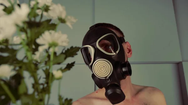 En ansiktslös man i gasmask med blommor. En oigenkännlig man med en naken överkropp i svart gasmask med en bukett färska vita blommor. Begreppet allergi och miljöförstöring — Stockfoto