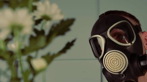 Mannen i gasmask tittar på blommor. Närbild av en hane i svart gasmask med prästkragar. Begreppet "plan för miljön eller allergi" — Stockfoto