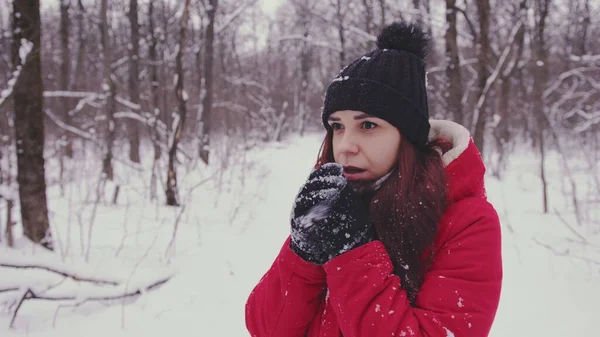 Joven mujer congelada en la cabecera y chaqueta roja. Mujer adulta calentando las manos con guantes con su aliento en clima frío. —  Fotos de Stock