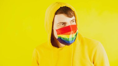 Sarı arka planda koruyucu gökkuşağı maskeli adam. Sarı kapüşonlu ve maskeli genç erkek portresi..
