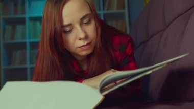 Güzel bir öğrenci büyük bir kitap okuyor. Düşünceli genç bir kadın elinde kitapla kanepede uzanıyor ve akşam karanlık bir odada kitap okuyor.