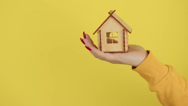 小さな木造の家を持つ若い女性の手。小さなおもちゃの家を保持作物認識できない人。新しいアパートや屋根のオーバーヘッドを購入する概念. — ストック動画