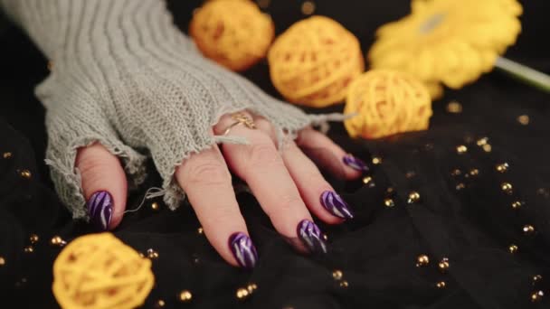 Voksne kvinder hånd i stilfuld strikket handske med lilla manicure på sort baggrund. Beskær uigenkendelig person med design på negle. Begrebet pleje og skønhed. – Stock-video