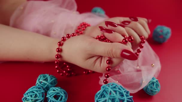 Fentről termés névtelen nő piros gyöngyökkel és piros manikűr piros háttér stúdióban dekoratív fonott labdák — Stock videók