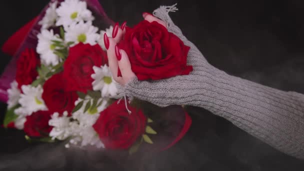Frauenhand mit roter Rosenknospe. Weibliche Hand in stylischem Strickhandschuh mit Blütenkopf auf schwarzem Hintergrund mit Blumenstrauß. — Stockvideo