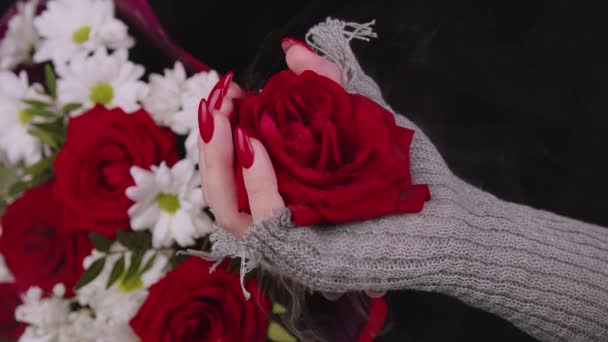 Tangan lebar dengan kuncup mawar merah. Tangan perempuan dalam sarung tangan rajutan bergaya dengan kepala bunga di latar belakang hitam dengan buket bunga. — Stok Video