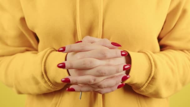 Część ciała młodej kobiety z rękami skrzyżowanymi w zamku. Uprawa nierozpoznawalna osoba w żółtej bluzie pokazujące gest splecionych palców z czerwonym manicure. — Wideo stockowe