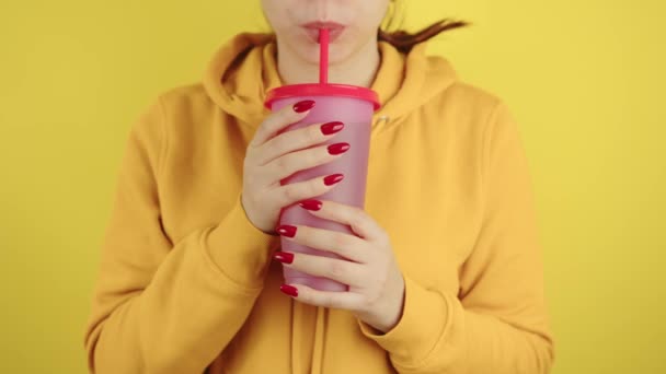 Część ciała kobiety z czerwonym manicure trzymając duży kubek. Uprawa nierozpoznana osoba picie przez słomkę napoju bezalkoholowego na żółtym tle. — Wideo stockowe