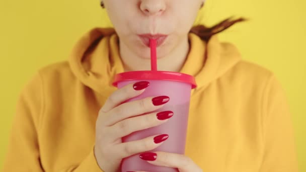 Część ciała kobiety z czerwonym manicure trzymając duży kubek. Uprawa nierozpoznana osoba picie przez słomkę napoju bezalkoholowego na żółtym tle. — Wideo stockowe