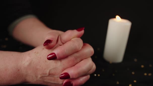 Crop woman praying with clasped hands. Crop unrecognizable religious female praying with folded hands at dark table with burning candle — Stock Video