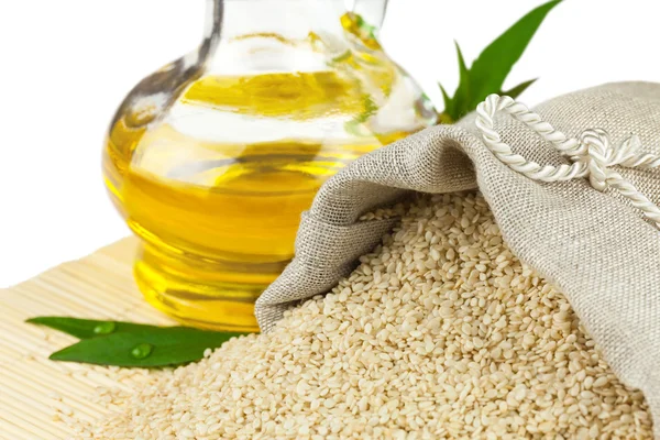 Sack of sesame seeds and glass bottle of oil on mat — Stock Photo, Image