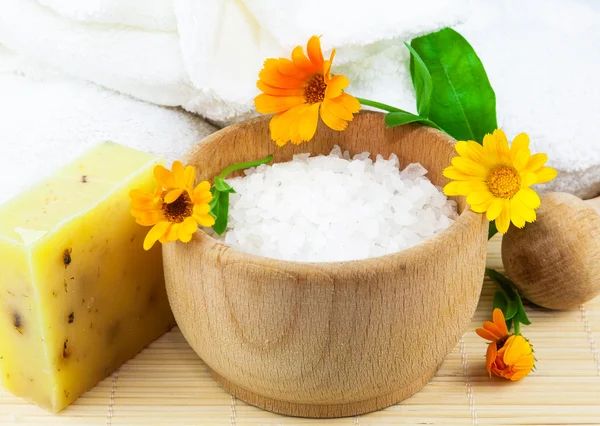 Wooden bowl with sea salt, soap, towels and marigolds — Stock Photo, Image