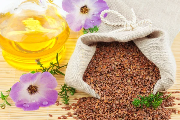 Sack of flax seeds and glass bottle of oil with flowers — Stock Photo, Image