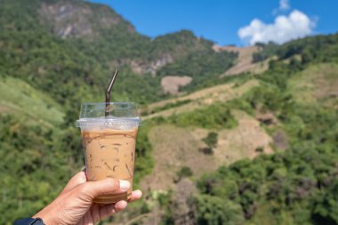 El soğuk espresso kahve bir bardak tutan Arka plan bulanık görünümleri ağaç ve Dağ