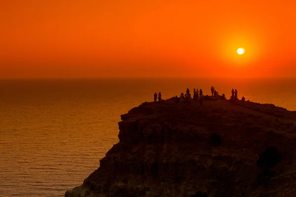 Gente siluetas en la puesta de sol en el acantilado sobre el mar — Foto de Stock