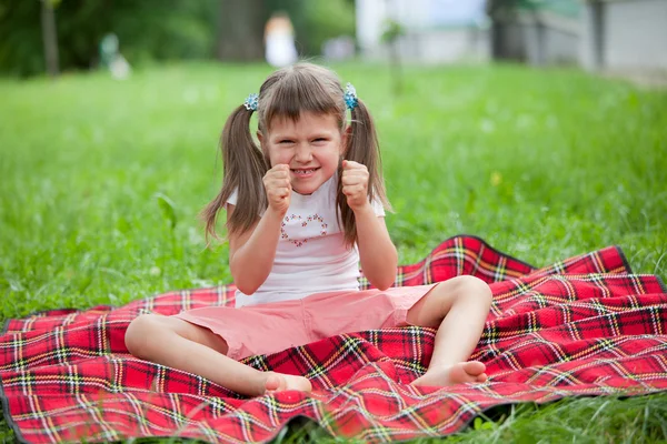 Little irritated girl preschooler sitting on plaid and grass — Stock Photo, Image