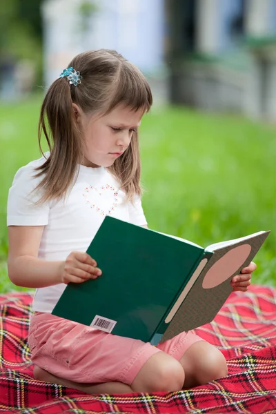 Pouco bonito menina pré-escolar com livro sobre xadrez no parque — Fotografia de Stock