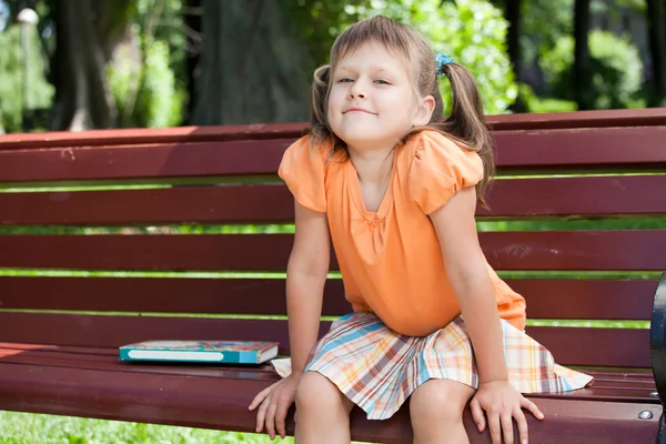 Liten söt leende flicka med boken på bänk — Stockfoto