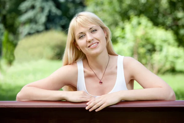 Joven mujer rubia alegre en el banco en el parque de verano — Foto de Stock