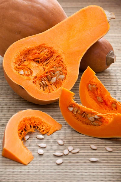 Ripe orange pumpkins, sliced segments and seeds on woven surface — Stock Photo, Image