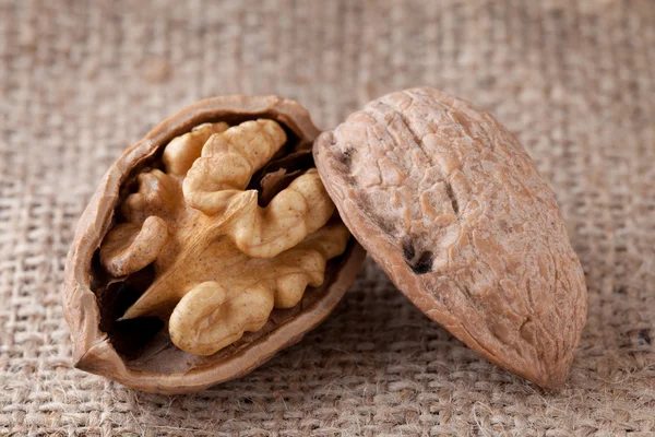 Macro cracked walnut, kernel inside, nutshell on sackcloth backg — Stock Photo, Image