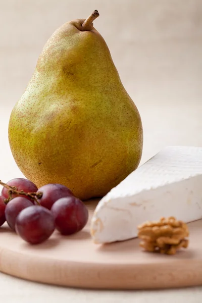 Grön päron, ost brie, valnöt, druvor på träplatta makro — Stockfoto