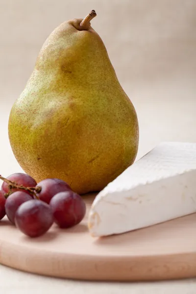 Pêra verde, queijo brie, uvas vermelhas na tábua de madeira macro — Fotografia de Stock