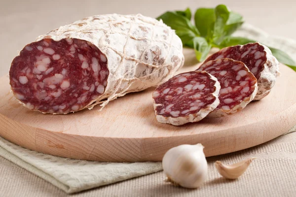 Traditionella skivad salami på träplatta med vitlök och örter — Stockfoto