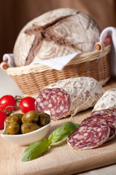 Slices salami on board, cherry tomatoes, olivas, bread in breadb — Stock Photo, Image