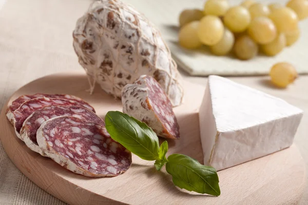 Traditionella skivad salami på träplatta med brie, druvor, bas — Stockfoto