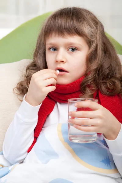 Little sick girl with scarf in bed is taking a pill — Stock Photo, Image