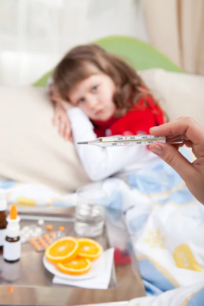 Klinisk termometer i hånden som viser feber og liten syk jente – stockfoto